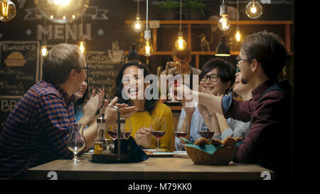 Vielfältige Gruppe von Freunde Feiern mit einem Toast und Heben Weingläser in der Feier. Schöne junge Leute haben Spaß in der stilvollen Bar/Restaurant. Stockfoto