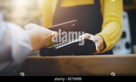Cafe Mitarbeiter Vertrieb Takeaway Kaffee zu einem Kunden, zahlt sich durch berührungslose Handy Kreditkarte System. Stockfoto