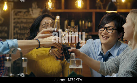 Vielfältige Gruppe von schönen jungen Menschen einen Toast und Clink angehoben Gläser mit verschiedenen Getränken in der Feier. Stockfoto