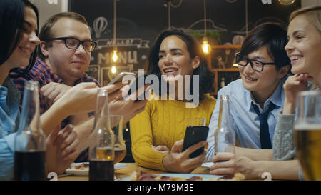In der Bar/Restaurant vielfältige Gruppe von Freunde haben gute Zeit Weitergeben von Bildern und Whatnot mit ihren Smartphones. Schöne Menschen in der stilvollen Bar Stockfoto