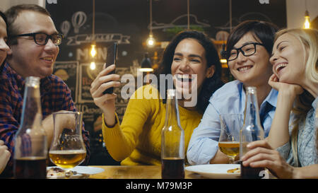 In der Bar/Restaurant Hispanic Frau macht Video Gespräch mit Ihren Freunden. Gruppe Schöne junge Menschen in der stilvollen Einrichtung. Stockfoto
