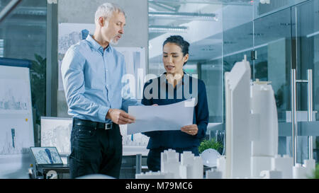 Zwei professionelle Männliche und Weibliche architektonischen Ingenieure arbeiten mit Blueprints, Diskutieren Gebäude Modell Design für das städtebauliche Projekt. Stockfoto