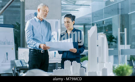 Zwei professionelle Männliche und Weibliche architektonischen Ingenieure arbeiten mit Blueprints, Diskutieren Gebäude Modell Design für das städtebauliche Projekt. Stockfoto