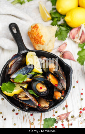 Leckere Muscheln in Weißwein mit Zitrone, Knoblauch, Kräuter und Gewürze in einer gusseisernen Pfanne. Baguette, Koriander und Pfeffer. Fisch und Meeresfrüchte. Muscheln in der Sie Stockfoto