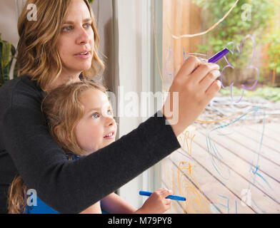 Eine Frau und ihr können Sie über das Fenster Markierungen in einem Fenster zu zeichnen Tochter. Stockfoto