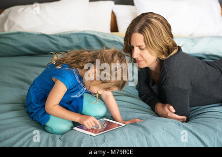 Eine Frau, die ihre Tochter Beobachten lernen, wie man mit einem ipad mini schreiben. Stockfoto