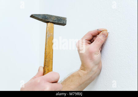 Die Hand des Mannes ist, einen Nagel in die Wand ein Bild zu hängen. Stockfoto