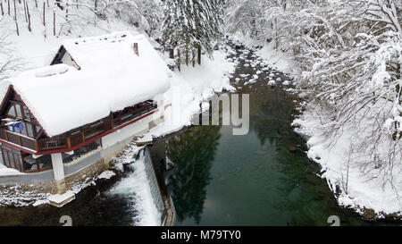 Luftaufnahme des Kamacnik Fluss bedeckt in tiefem Schnee mit einem Haus und Wasserfall, Kroatien Stockfoto