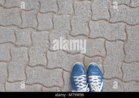 Paar blaue gebootet Füße mit weißen Schnürsenkeln auf gemusterten Pflastersteine. Die Füße sind durch die Kante mit dem Raum um sie herum. Stockfoto