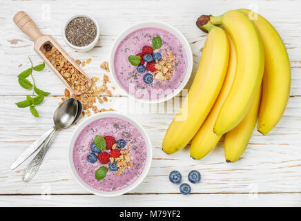 Gesunde leckere Smoothies von Banane und frischen Beeren Himbeeren und Blaubeeren Müsli mit Chia Samen und Minze in Weiß Schüssel Stockfoto