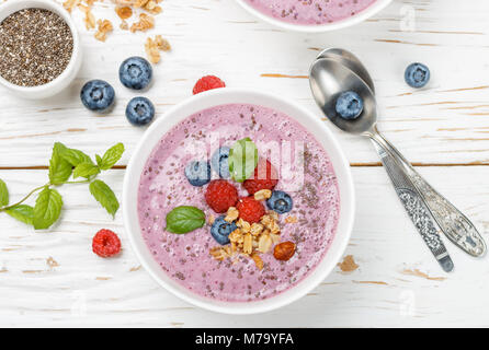 Gesunde leckere Smoothies von Banane und frischen Beeren Himbeeren und Blaubeeren Müsli mit Chia Samen und Minze in Weiß Schüssel Stockfoto