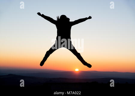 Eine junge Frau zeigt fröhliche Gesten in der untergehenden Sonne von Dartmoor, Großbritannien. Stockfoto