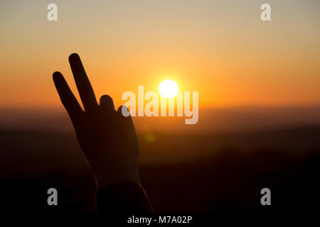 Ein friedenszeichen Geste wird von der untergehenden Sonne in Dartmoor, Großbritannien Silhouette Stockfoto