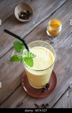 Gelbwurz Lassie oder Lassi aus Glas - gesunden probiotischen Indischen kaltes Getränk aus Quark (Joghurt), Milch, Gewürzen und Zucker. Gelbwurz Smoothie auf Holz, Stockfoto