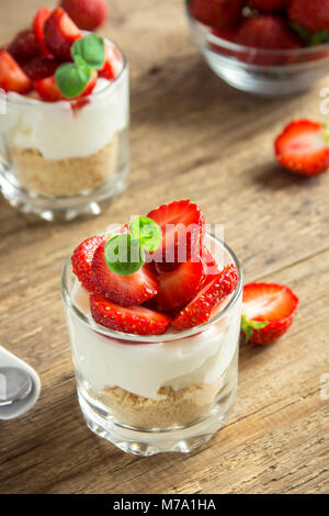 Strawberry cheesecake in Gläsern mit frischen Erdbeeren und Sahne Käse auf Holz- Hintergrund. Gesunde hausgemachte Desserts. Stockfoto