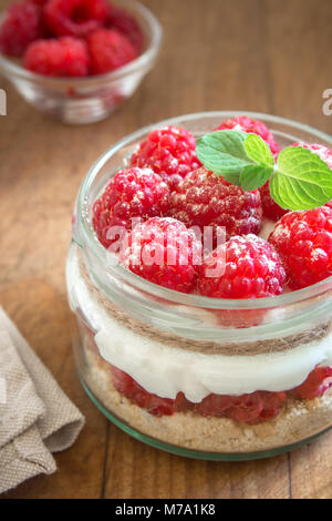 Raspberry cheesecake in Glas Glas mit frischen Himbeeren und Sahne Käse auf Holz- Hintergrund. Gesunde hausgemachte Sommer berry 2-in-1-Dessert. Stockfoto