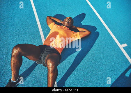 Junge athletische afrikanischer Mann in Sportkleidung liegen auf dem Wege einer Laufstrecke eine Pause vom Training Stockfoto