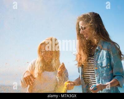 Zwei schöne glückliche Mädchen feiern Holi Festival durch das Werfen von bunten Pulver in die Luft und lacht. Sie sind durch das Meer und haben viel Spaß. Stockfoto