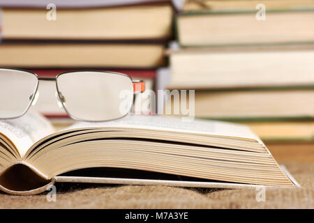 Ein aufgeschlagenes Buch mit Brille liegen auf einem Jute-Matte mit einem unscharfen Hintergrund Stockfoto