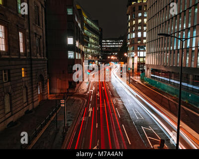 Die leichte Wanderwege auf der Bürogebäude Hintergrund in der Nacht als vorbeifahrende Autos auf Upper Thames Street in London, UK. Grüne und rote Ampeln. Stockfoto