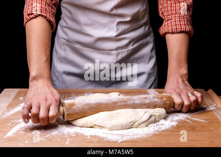 Eine Frau wird mit dem Nudelholz den Teig zu Rollen. Stockfoto