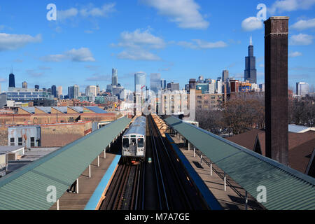 Eine grüne Linie Zug Richtung Westen auf dem Lake St. Hochbahn an der Ashland Station mit der Skyline von Chicago über den Horizont ausgebreitet. Stockfoto