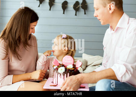 Eltern mit einem kleinen niedlichen Tochter. Mädchen versucht, den Kuchen mit ihren Finger Stockfoto