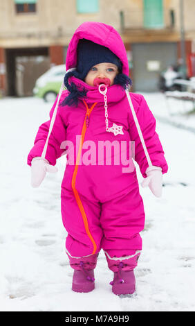 Adorable Kleinkind Baby Mädchen in einem magenta Schnee Anzug spielen auf dem Schnee. Stockfoto