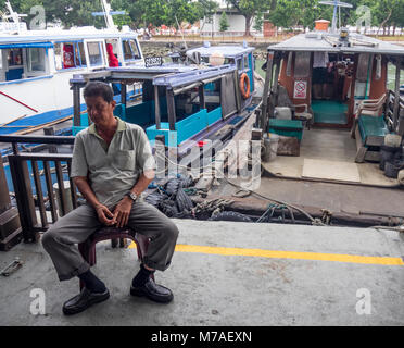 Ein Boot Besatzungsmitglied auf einem Stuhl sitzend Warten auf Passagiere aus Singapur in die Insel Pulau Ubin durch Bumboat oder dem Wassertaxi. Stockfoto