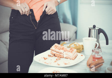 Porträt der jungen Frau, die versuchen, zip up Hosen in der Nähe des Tisches mit pie Stockfoto