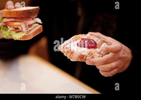 Mitte Schnittansicht eines Mannes hält eine Sandwich mit einem Plundergebäck Stockfoto