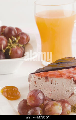 Nahaufnahme von zwei Scheiben Käsekuchen mit glasierten Trauben und Orangensaft Stockfoto