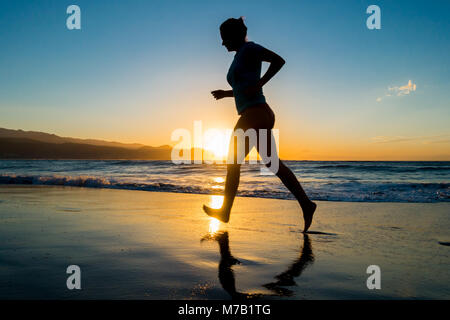 Frau Jogging am Strand bei Sonnenuntergang. Stockfoto