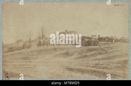 Ein Foto eines Lagers mit kleinen Hütten, die um ein größeres zentrales Gebäude angeordnet sind. Dieses Bild, das Teil der Sammlung Library of Congress ist, zeigt eine ländliche Lagerumgebung mit Hütten in kreisförmiger Anordnung. Stockfoto