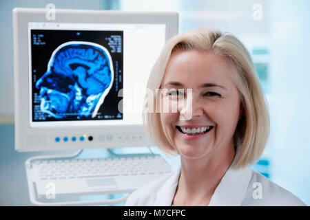 Ärztin mit MRT-Scan des Gehirns lächelnd auf dem Bildschirm Stockfoto