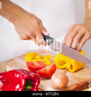 Man schneidet eine gelbe Paprika und Tomaten Stockfoto