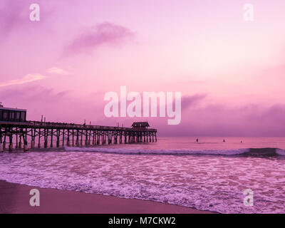 Sonnenaufgang über einem Pier an einem Strand in Florida erzeugt einen rosafarbenen Farbton über den Himmel. Stockfoto