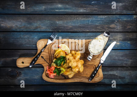 Fisch und Chips mit Sauce Tartar mit Besteck serviert. Stockfoto