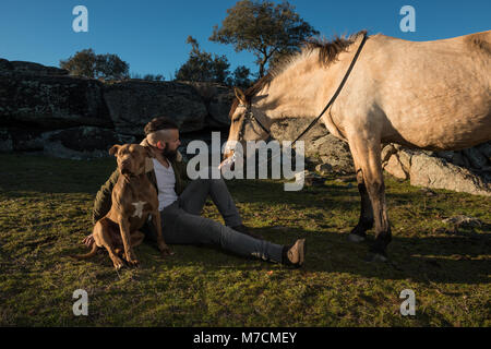Ein junger Dompteur mit seinem pitbull Hund und seinem Pferd in der Landschaft in Cáceres, Extremadura, Spanien Stockfoto