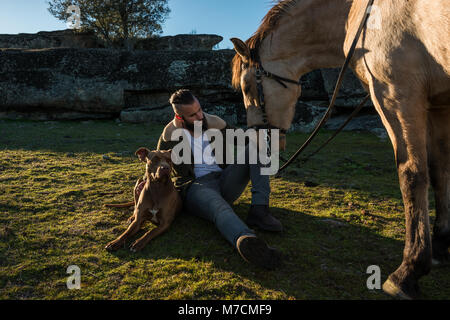 Ein junger Dompteur mit seinem pitbull Hund und seinem Pferd in der Landschaft in Cáceres, Extremadura, Spanien Stockfoto