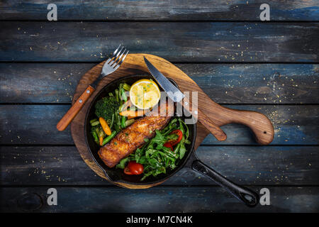 Gegrilltes Lachsfilet in einer Pfanne, Gemüse, Rucola mit Zitrone. Stockfoto