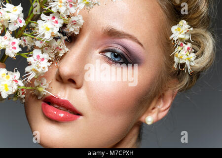 Schöne blonde junge Frau in Weiß top mit Blumen im Haar holding Zweig der blühenden Kastanien Blumen. studio Beauty Shot. kopieren. Stockfoto