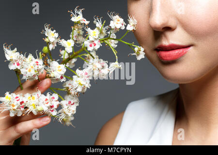 Schöne blonde junge Frau in Weiß top mit Blumen im Haar holding Zweig der blühenden Kastanien Blumen. studio Beauty Shot. kopieren. Stockfoto