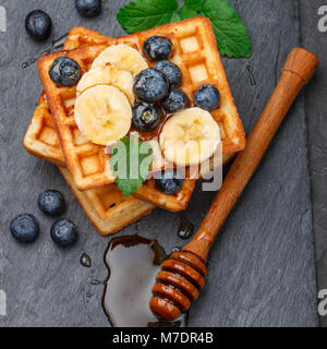 Traditionelle belgische Waffeln mit Blaubeeren, Banane und Honig auf schwarzem Schiefer Platte. Gourmet Frühstück. Selektiver Fokus Stockfoto
