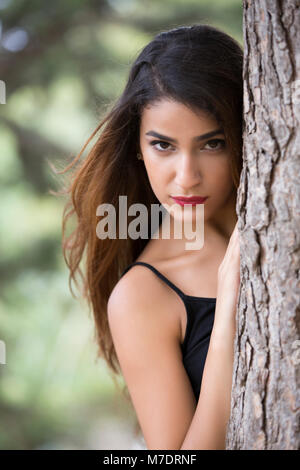 Schöne junge Frau hinter einem Baum Stockfoto