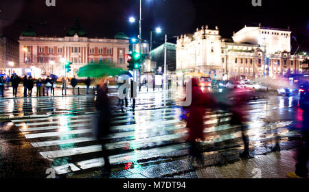Blurry Menschen Silhouetten Überqueren der Straße in Bewegungsunschärfe in regnerischen Nacht Stockfoto