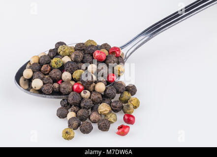 Close-up einen Löffel der würzigen Pfefferkörner. Piper nigrum. Die bunte Mischung der verschiedenen Pfefferkörner auf dem Löffel teilweise auf weißem Hintergrund verschüttet. Stockfoto