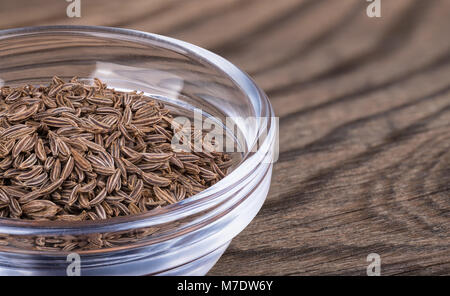 Close-up von Kümmel in Glas auf vintage Tabelle. Carum carvi. Braun getönten Hintergrund mit Kümmel Gewürz in die schöne transparente Schüssel auf Holz. Stockfoto