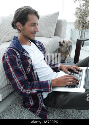 Moderne Kerl mit einem Laptop auf den Boden neben das Sofa Stockfoto