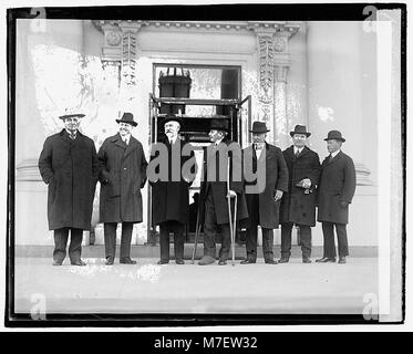 Ein Schwarzweiß-Foto, das sieben Männer zeigt, die am 6. Dezember 1920 vor einem Gebäude standen. Das Bild fängt einen Moment des Alltags aus dem frühen 20. Jahrhundert mit den Männern in formeller Kleidung ein. Stockfoto